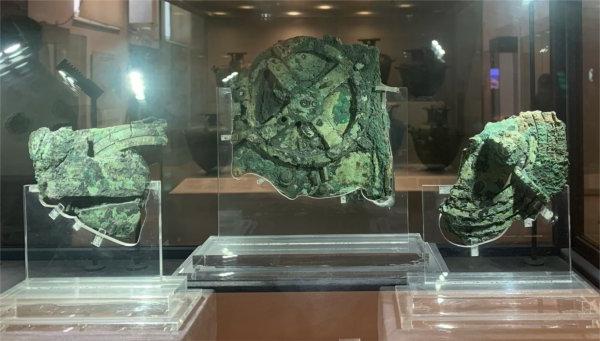 An artifact in three pieces, with a green coloring, is seen through a glass box.